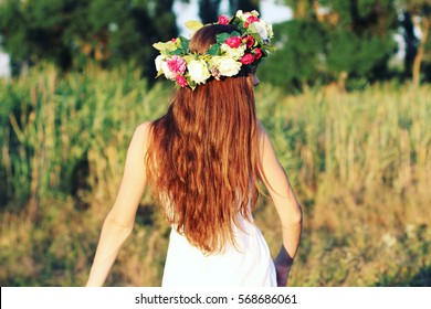 Woman in white dress standing in field wearing flower crown. Young forest inspired bride, bohemian girl