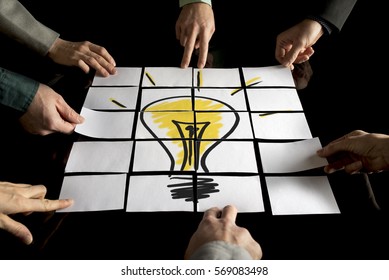 Brainstorming- und Teamwork-Konzept mit einem Team von sieben Geschäftsleuten, die Weißbücher arrangieren, die eine gelbe Glühbirne auf einem schwarzen Tisch bilden.