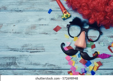 një parukë e kuqe, një palë syze të zeza false me vetulla, një hundë dhe një mustaqe që formojnë fytyrën e një burri në një sipërfaqe druri fshatar blu plot me konfeti dhe një hapësirë ​​bosh në të majtë