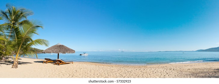 Panorama de playa tropical con tumbonas, sombrillas, botes y palmeras