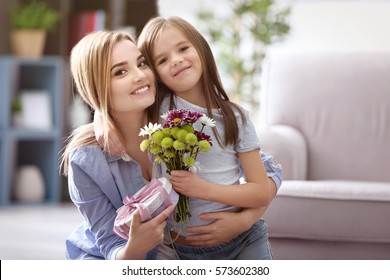 Schöne junge Frau mit Geschenk und Blumenstrauß von ihrer Tochter. Muttertagskonzept