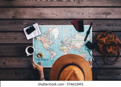 Mujer joven planeando vacaciones usando mapa mundial y brújula junto con otros accesorios de viaje. Turista con sombrero marrón mirando el mapa del mundo.