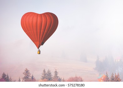 Red air balloon in shape of heart fly above forest in foggy morning. Romantic postcard background on Valentine's Day. Adventure trip for couples. Sport and recreation travel theme. Nature background