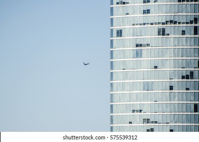 Pemandangan abstrak dari fasad gedung pencakar langit modern dengan jendela tertutup dan terbuka dengan latar belakang langit biru jernih. Sebuah pesawat terbang tepat ke dalam gedung, sepertinya akan jatuh di gedung bertingkat