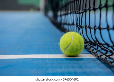 青いハードコートと黒いネットに黄色のテニスボール