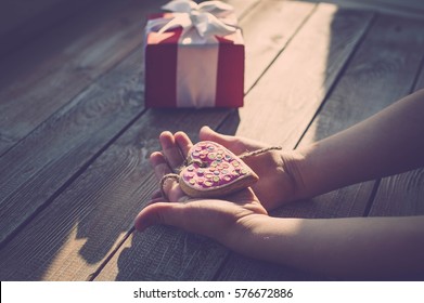 Kinderhände halten Kekse in Herzform auf einer Holztischplatte. Sonnenlicht. Ein Konzept zum Muttertag. Vintage-Tonung.