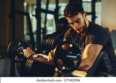 Knappe man doet biceps opheffing barbell op bankje in een sportschool