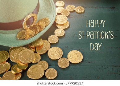 Topi leprechaun Happy St Patricks Day dengan koin cokelat emas dengan latar belakang kayu hijau bergaya vintage dengan teks dan menerapkan filter pudar gaya retro.