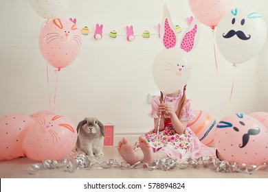 Bé gái xinh xắn trong chiếc váy hồng và chiếc mũ lưỡi trai có chú thỏ đang cười. Dịp. Lễ Phục sinh. Thời thơ ấu.