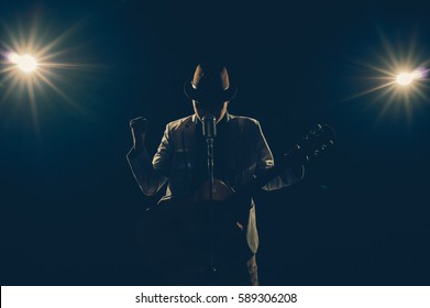 アジアのミュージシャンが歌を歌い、ギターを弾き、黒い背景にマイクを持ち、スポットライトとレンズフレア、音楽的コンセプト