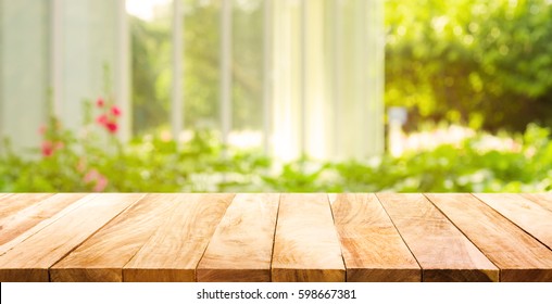 Mesa de madera vacía sobre verde abstracto borroso del jardín y la casa en el fondo de la mañana. Para exhibición de productos de montaje o diseño visual clave de diseño