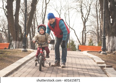 First bike. Father help his toddler daughter ride a bicycle. Spending Family time together - father and son. Sport concept. Child on bicycle at asphalt road in sunny day. Toddler preschool boy protect