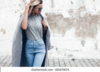 Cô gái hipster mặc áo phông xám trống, quần jean và áo khoác tạo dáng trên bức tường đường gồ ghề, phong cách quần áo thành thị tối giản, mô hình cho cửa hàng in áo phông