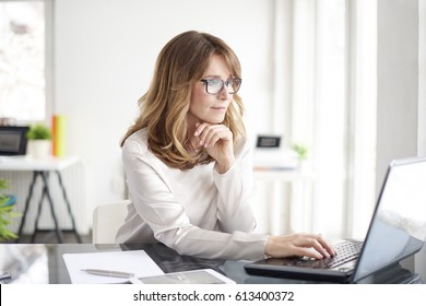 Disparo de una atractiva mujer de negocios madura que trabaja en una computadora portátil en su estación de trabajo.