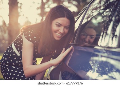 Opgewonden jonge vrouw en haar nieuwe auto buiten met zonovergoten bos op de achtergrond.