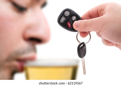 Betrunkenes Fahrkonzept mit einer Hand, die einige Autoschlüssel und einen Mann hält, der Bier im Hintergrund trinkt. Geringe Schärfentiefe.