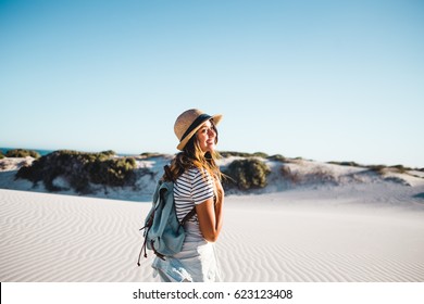 Young female exploring sandy beach with hat and backpack