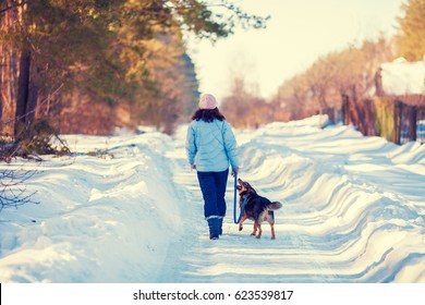 Young woman with her dog walking on the snowy  road in village back to camera