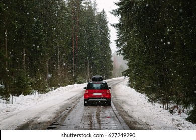 Coche rojo con portaequipajes conduciendo por un camino forestal en invierno, fuertes nevadas. El concepto de viajar en coche.