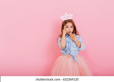 Niña bonita sorprendida en falda de tul con corona en la cabeza expresando aislado sobre fondo rosa. Increíble princesita linda en el carnaval. Lugar para el texto