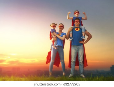 Mutter, Vater und ihre Töchter spielen im Freien. Mama, Papa und Kinder Mädchen in den Kostümen eines Superhelden. Konzept der Superfamilie.