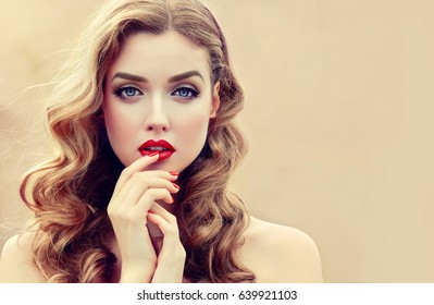Beautiful blonde model girl with long curly hair . Hairstyle wavy curls . Red lips and nails manicure . Fashion , beauty and make up portrait