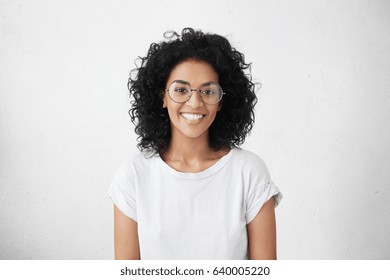 Indoor portrait of beautiful brunette young dark-skinned woman with shaggy hairstyle smiling cheerfully, showing her white teeth to camera while feeling happy and carefree on her first day-off