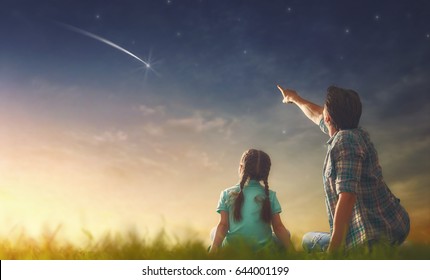 Father and his daughter are looking at falling star.