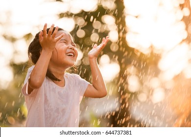 ヴィンテージ色のトーンで夕方の日差しの中で雨と遊ぶのを楽しんでいる幸せなアジアの小さな子供の女の子