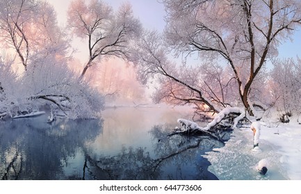 Winterweihnachtslandschaft in den rosa Tönen mit ruhigem Winterfluss, umgeben von Bäumen. Winterwald auf dem Fluss bei Sonnenuntergang. Landschaft mit schneebedeckten Bäumen, schöner gefrorener Fluss mit Reflexion im Wasser
