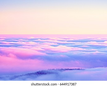 ピンクのオレンジ色の太陽が霧深い冬の山の上に昇り、霧が輝いています。谷のクリーミーな霧の上の山の頂上。