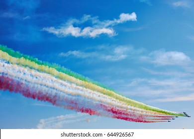 航空ショーの航空戦闘機は、雲のある青い空を背景に、色とりどりの明るい煙の軌跡を持つ幾何学的図形の形で飛行します。空気性能