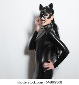 美しい支配的なブルネット ヴァンプ ゴス愛人邪悪な少女ラテックス ドレス、先端のとがった襟と bdsm 黒革フェチ猫マスク ポーズ白い背景に