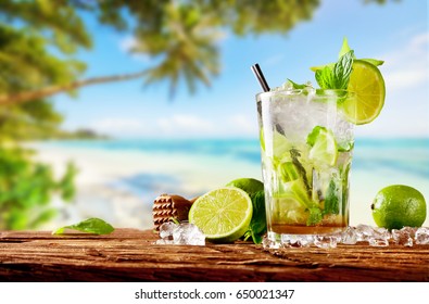 Bebida fresca de mojito colocada en tablones de madera, playa tropical borrosa en el fondo. Bebidas de verano y fondo de vacaciones en la playa.
