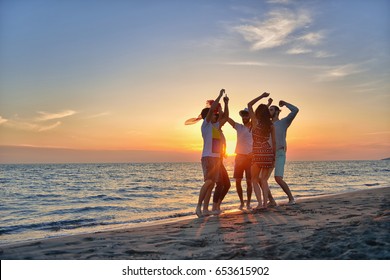 美しい夏の夕日のビーチで踊る幸せな若者のグループ