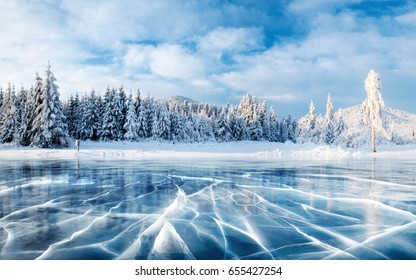 Grietas en la superficie del hielo azul. Lago congelado en las montañas de invierno. Está nevando. Las colinas de pinos. Cárpatos Ucrania Europa.