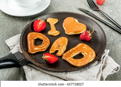 Vatertag feiern. Frühstück. Die Idee für ein herzhaftes und leckeres Frühstück: Pfannkuchen in Form von Glückwünschen - I love dad. In einer Bratpfanne, Kaffeetasse und Erdbeeren. Platz kopieren