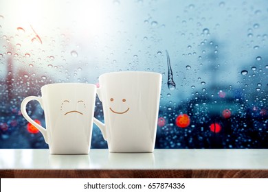 Aanmoedigingsconcept, vriend van koffiemok met verdriet huilend gezicht cartoon en vriendelijkheid blij gezicht in de kamer, wazig stadslicht en regendruppel in de stad als buitenaanzicht door glazen raam