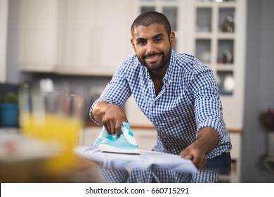 自宅の家庭の台所で布にアイロンをかける若い男の笑顔の肖像画