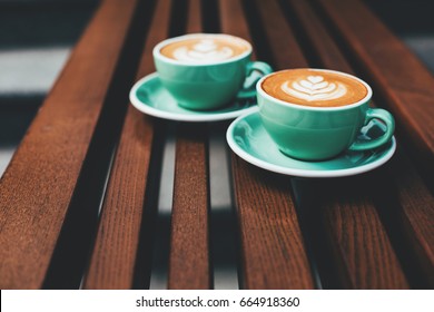 Dua cangkir cappuccino dengan seni latte di latar belakang kayu. Busa yang indah, cangkir keramik hijau, toning bergaya, tempat untuk teks.