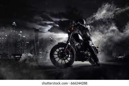 夜の男性ライダーとハイパワー バイク チョッパーのディテール。ドバイの近代都市と背景にバックライト付きの霧。