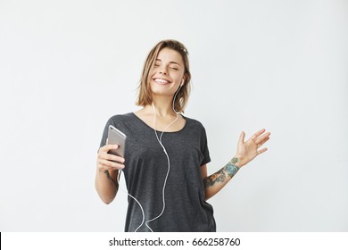 Cheerful young pretty girl smiling listening music in headphones dancing over white background. Closed eyes.