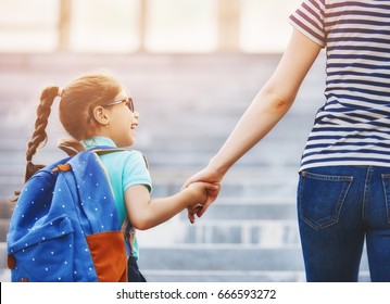 Padres y alumnos de primaria van de la mano. Mujer y niña con mochila detrás de la espalda. Comienzo de clases. Primer día de otoño.