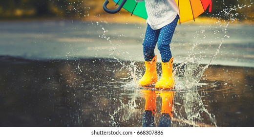 Pies de niño con botas de goma amarillas saltando sobre un charco bajo la lluvia