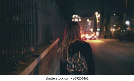 Back view of brunette woman walking near the road at the traffic time. Girl goes through the city late at night alone.