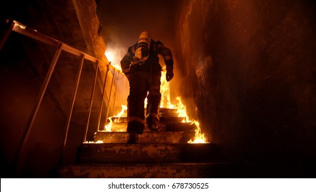 Starker und mutiger Feuerwehrmann, der im brennenden Gebäude die Treppe hinaufgeht. Treppen brennen mit offenen Flammen.