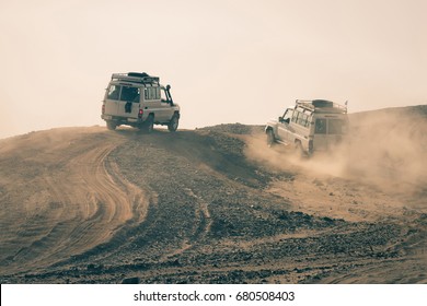 Cars driving in dusty desert on white sky background. Safari trip on 4x4 jeeps. Dune bashing. Offroad adventure. Extreme activity. Travel, travelling. Summer vacation