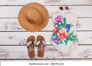 Set of women beach accessories. One-piece floral swimwear, straw hat, sandals and sunglasses on wooden background.