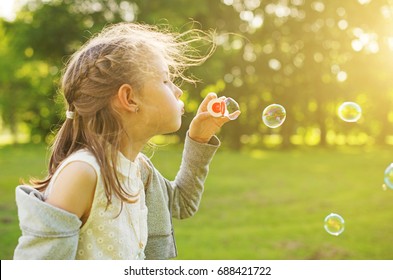 Little girl blowing soap bubbles in the park.