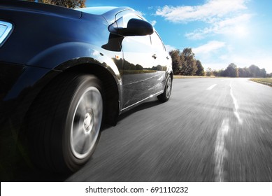Zwarte auto rijdt snel op een weg tegen de blauwe lucht op het platteland